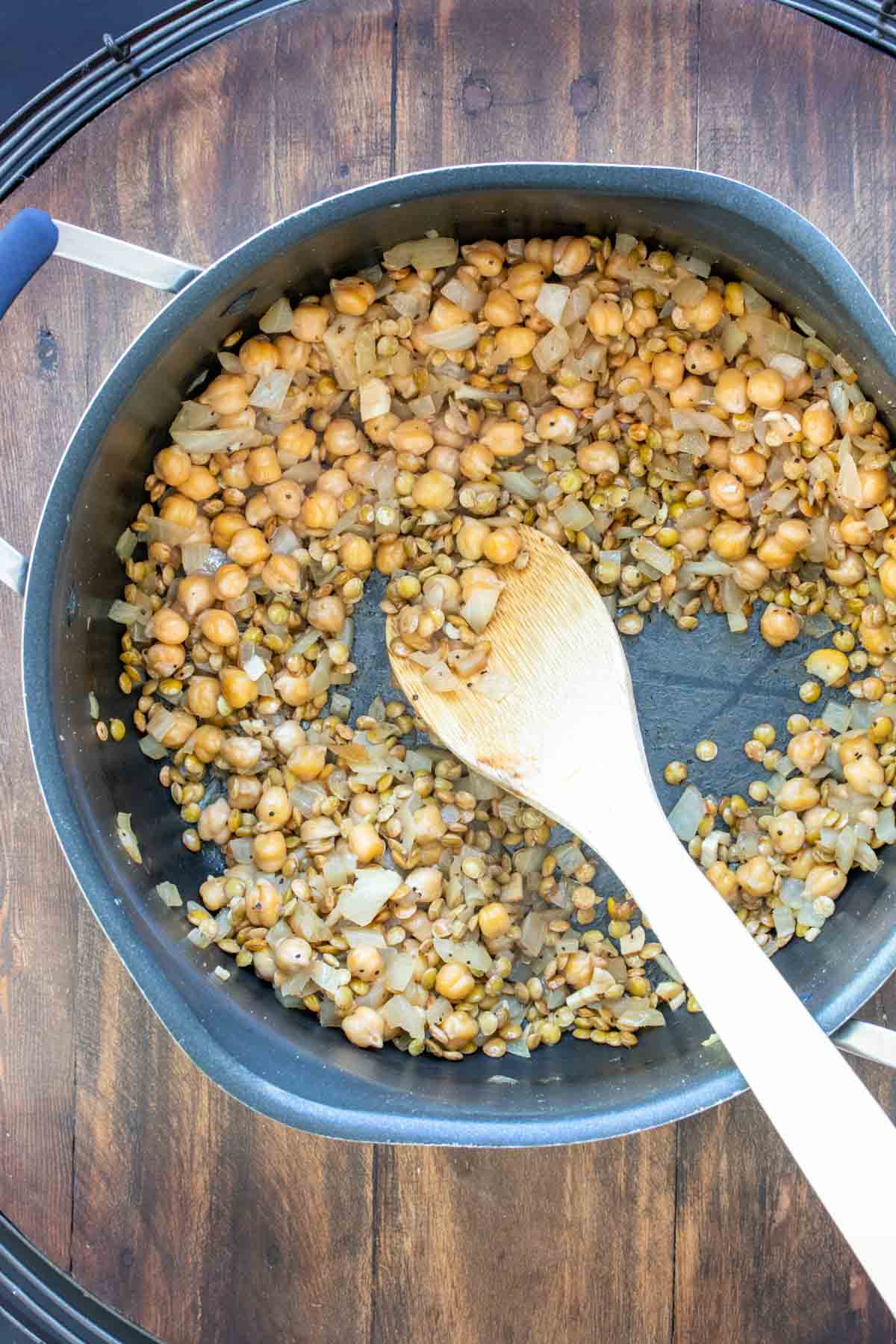 Wooden spoon mixing chickpeas, lentils and onions in a pot
