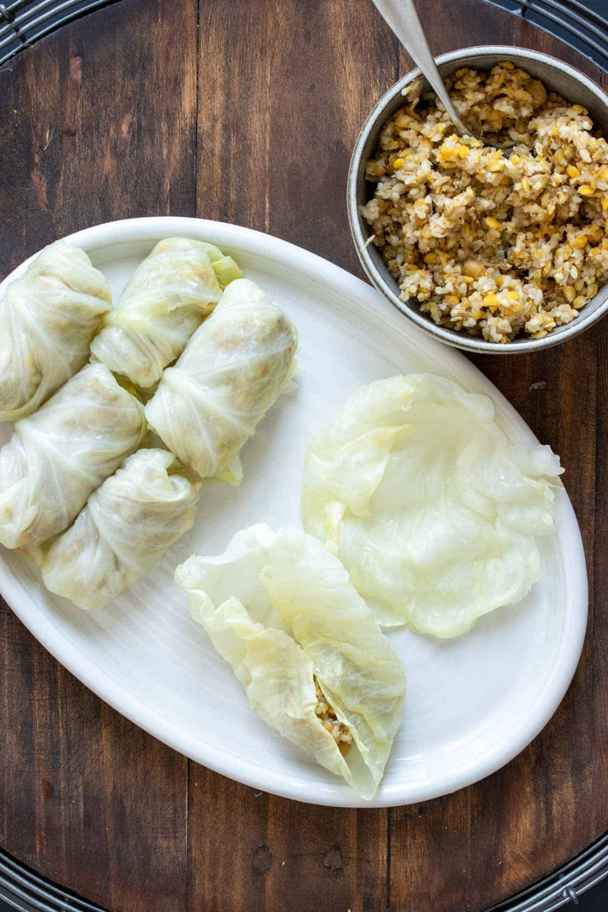 White platter with stuffed cabbage lined up while some is getting stuffed