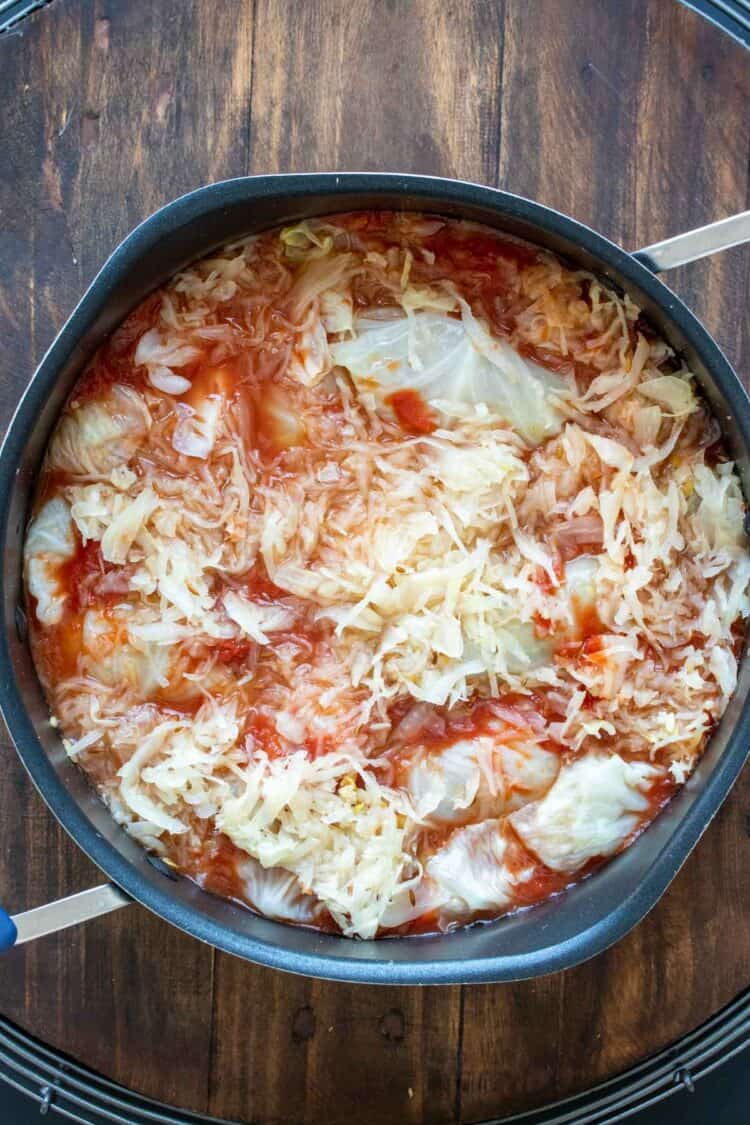 Top view of a pot filled with cabbage rolls and topped with tomato sauce and sauerkraut