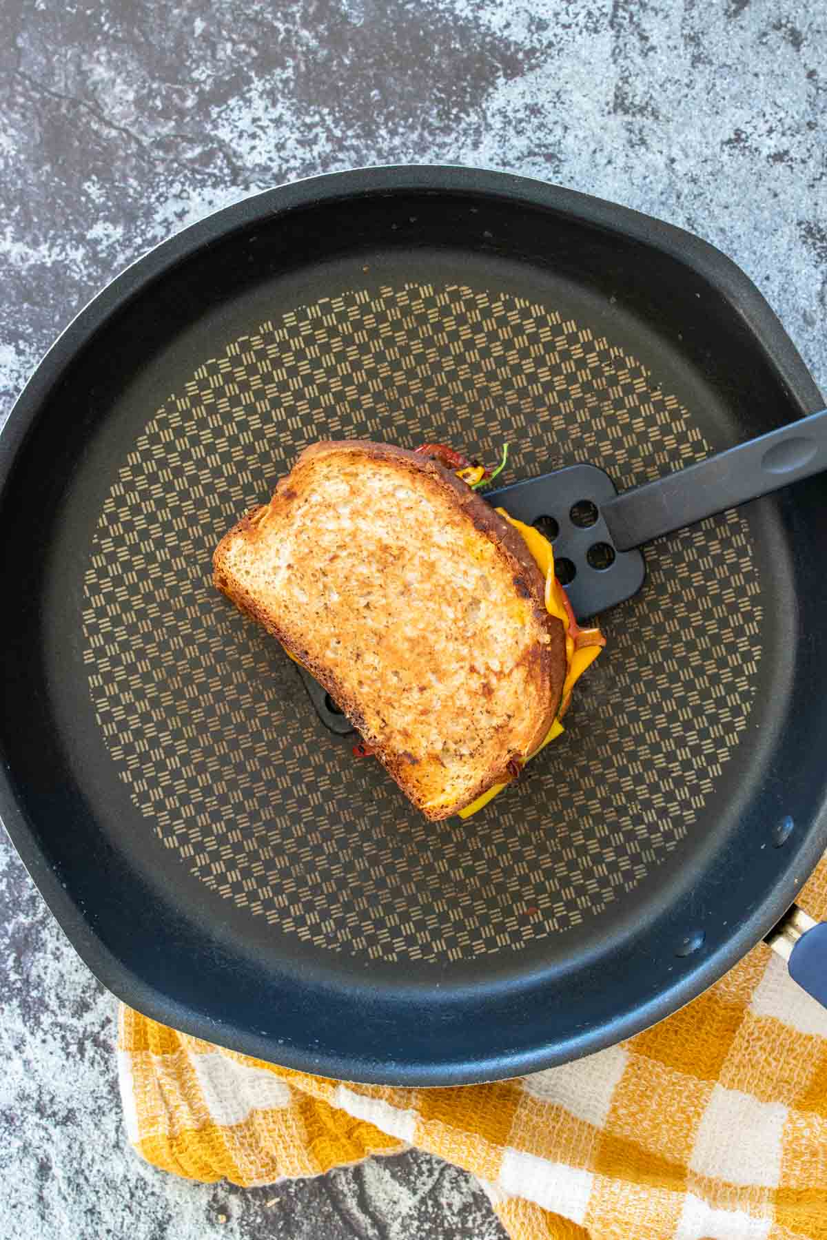 A spatula holding a grilled cheese sandwich over a black pan