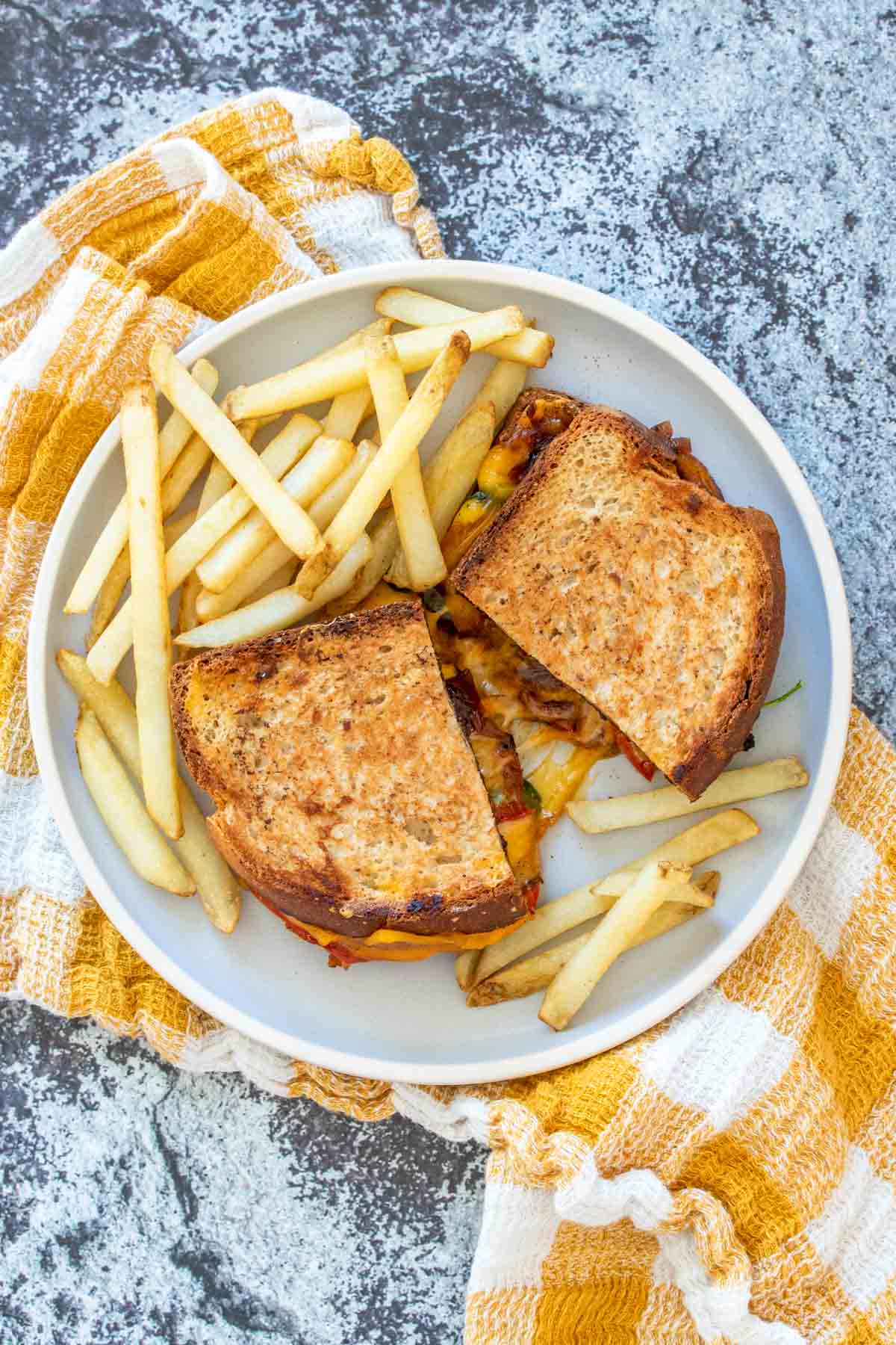 A grilled cheese sandwich on a plate cut in half and spread apart with cheese and veggies oozing out next to fries.