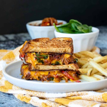 Two halves of a veggie grilled cheese stacked on a plate next to french fries