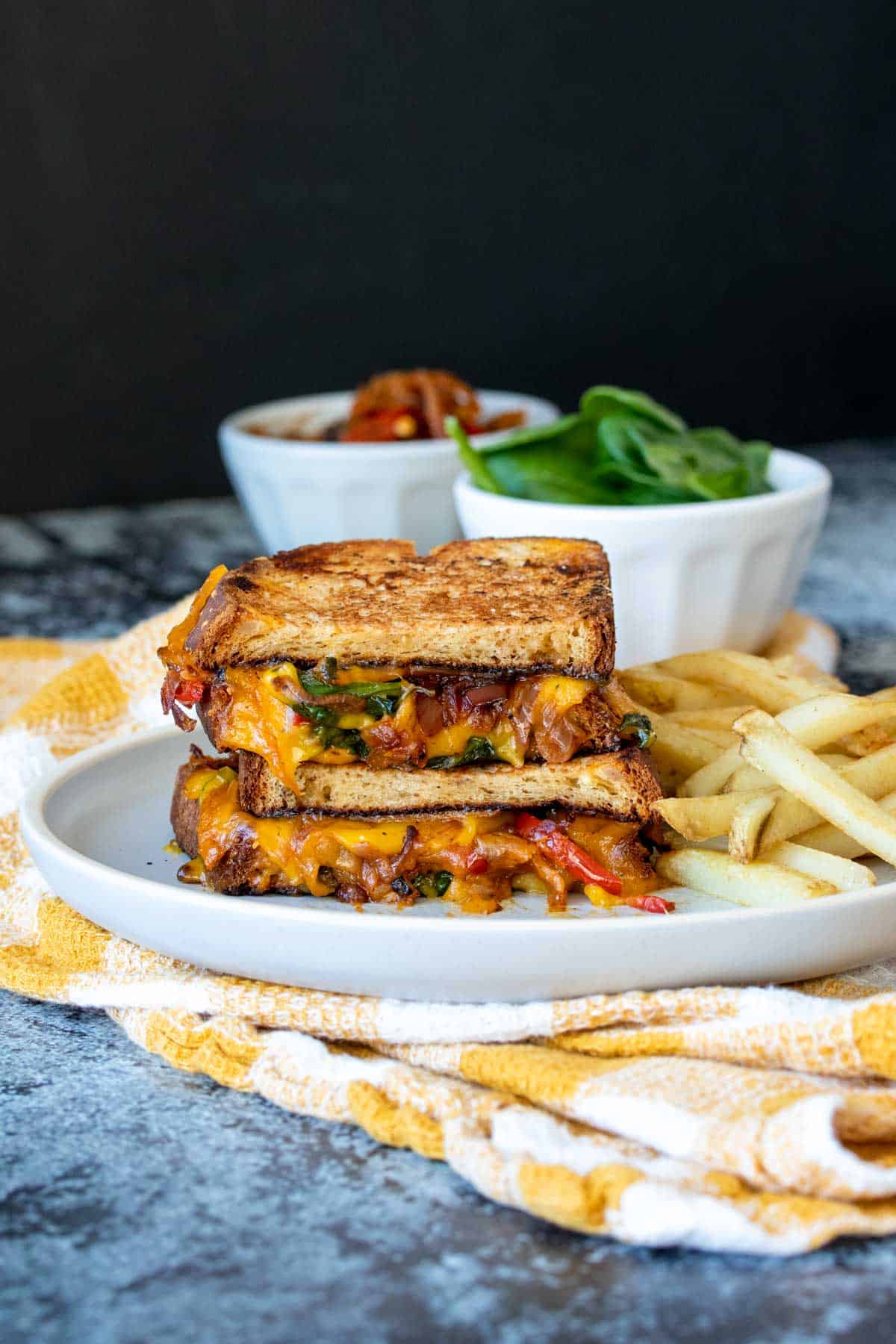 Two halves of a veggie grilled cheese stacked on a plate next to french fries