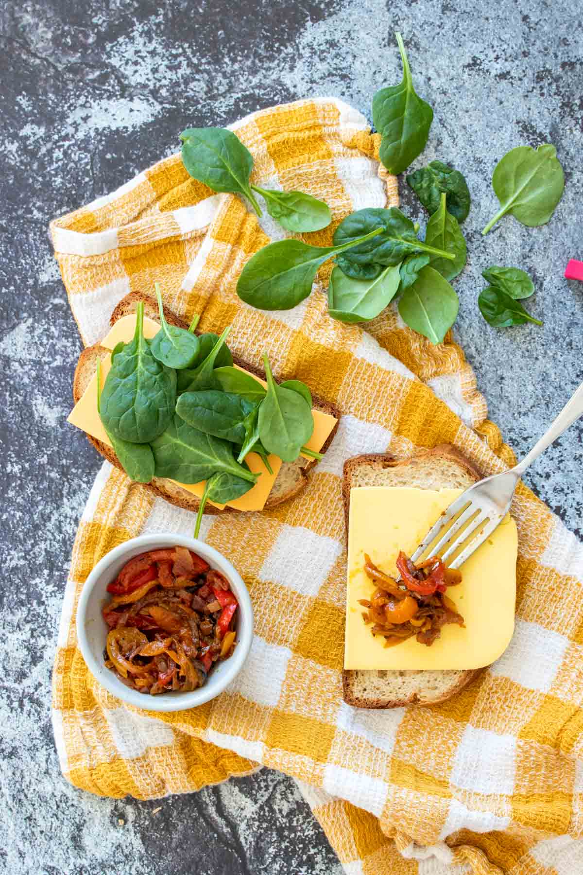 Overhead view of two sliced of bread with cheese, spinach and sauteed peppers on top