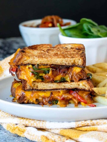 A grey plate on a yellow checkered towel with a stack of veggie grilled cheese on it.