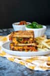 A grey plate with a stacked veggie grilled cheese on a grey surface with a yellow towel.