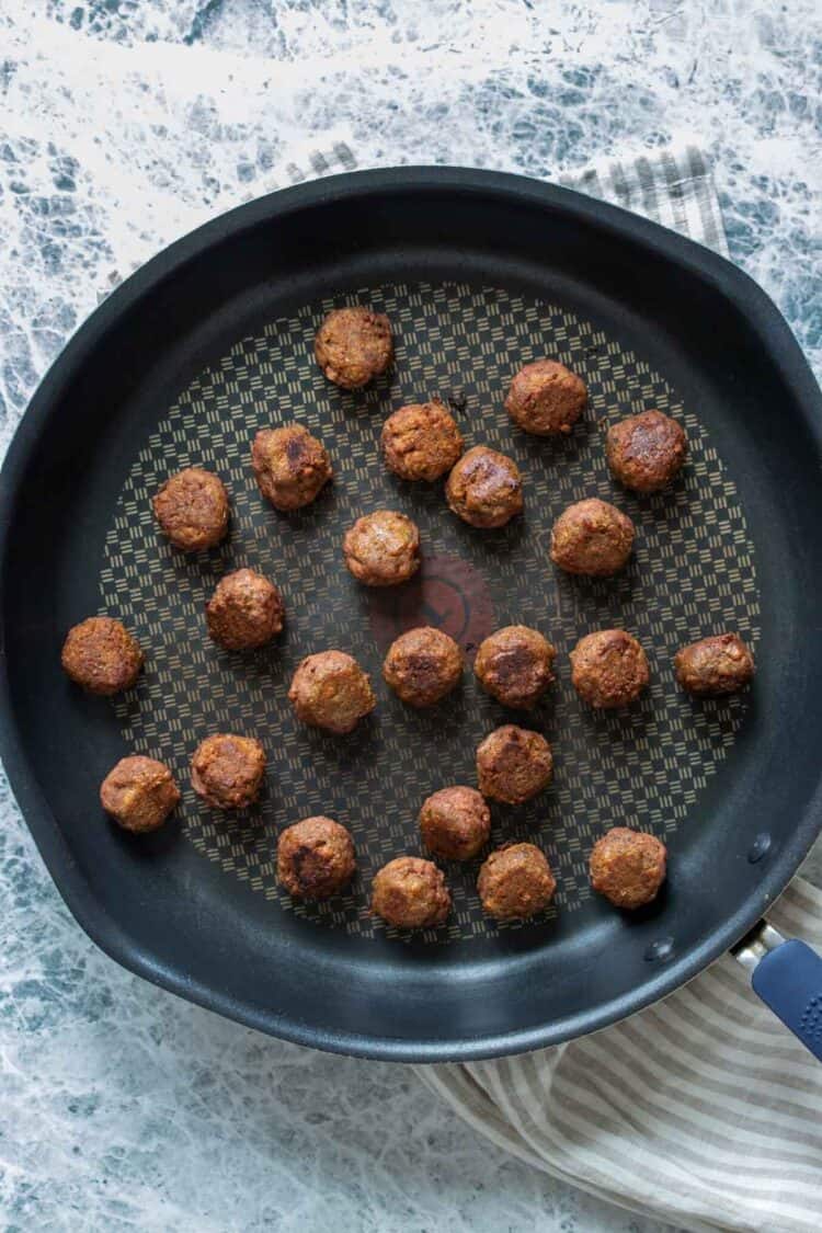 A frying pan on a striped towel with small meatballs cooking in it