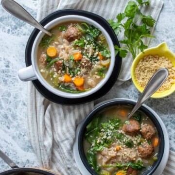 Two bowls, black and white, on top of the opposite colored plates with a veggie, orzo and meatball soup in them