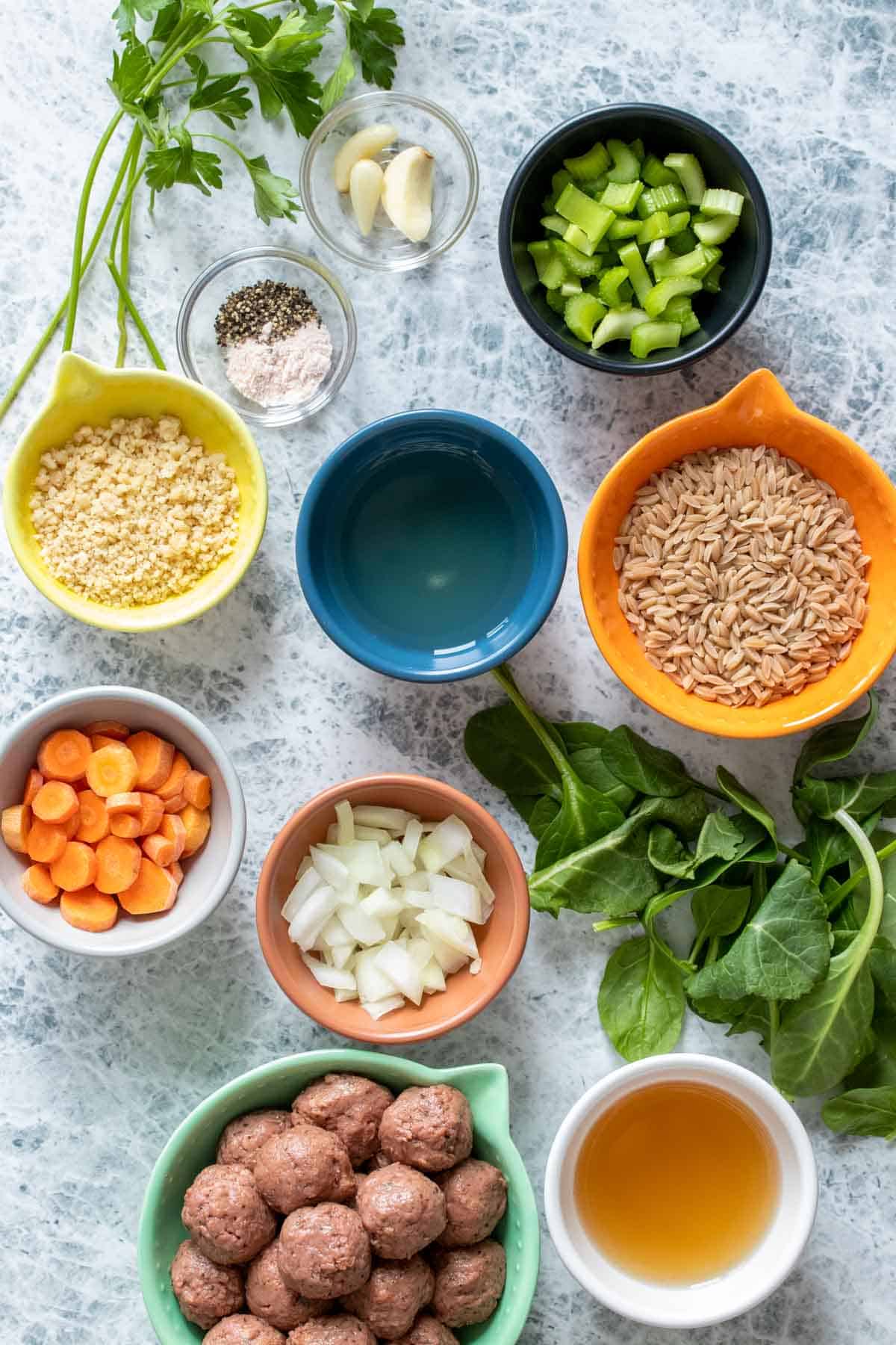 Top view of different colored bowls on a marbled surface with ingredients needed for Italian wedding soup