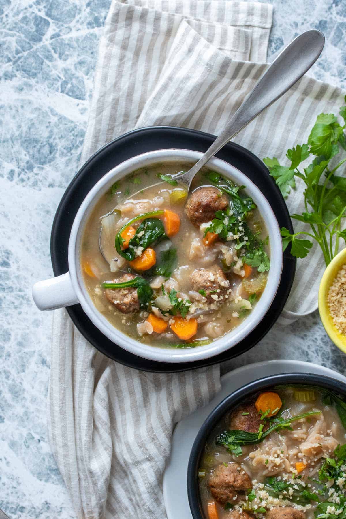 A spoon getting a scoop of Italian wedding soup from a white soup bowl on a black plate