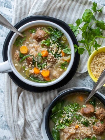 A set of two bowls on plates, all black and white, on a striped towel filled with Italian wedding soup