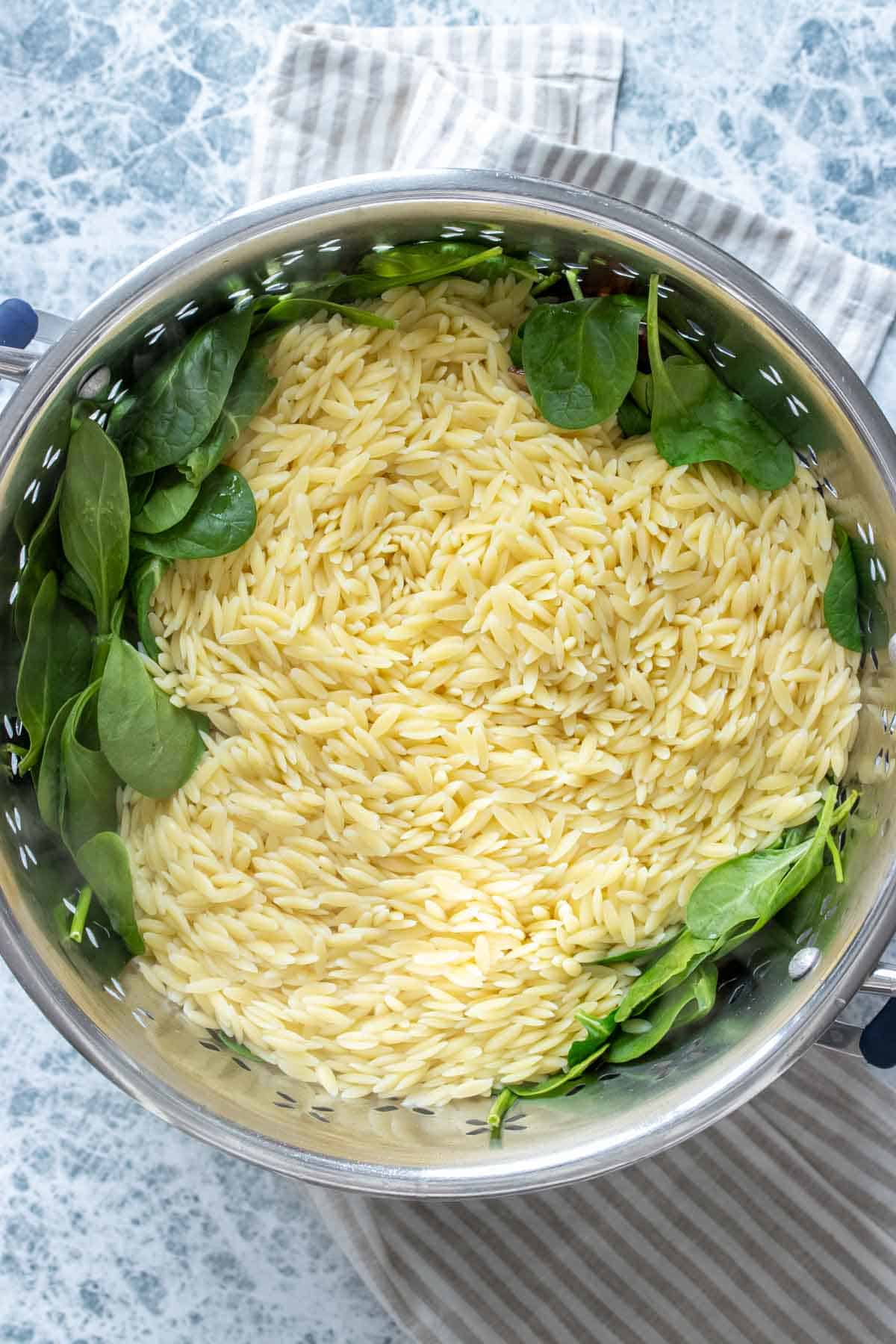 Top view of a pasta strainer with cooked orzo over spinach inside