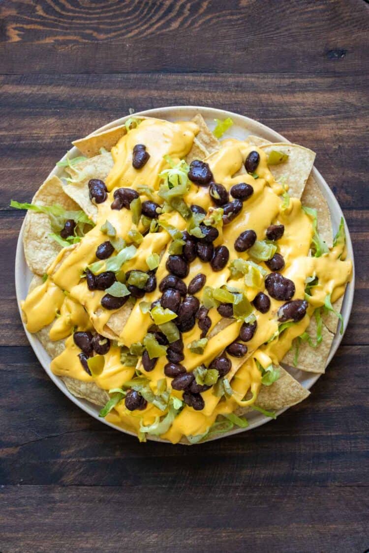 A plate with tortilla chips, shredded lettuce, cheese sauce and black beans