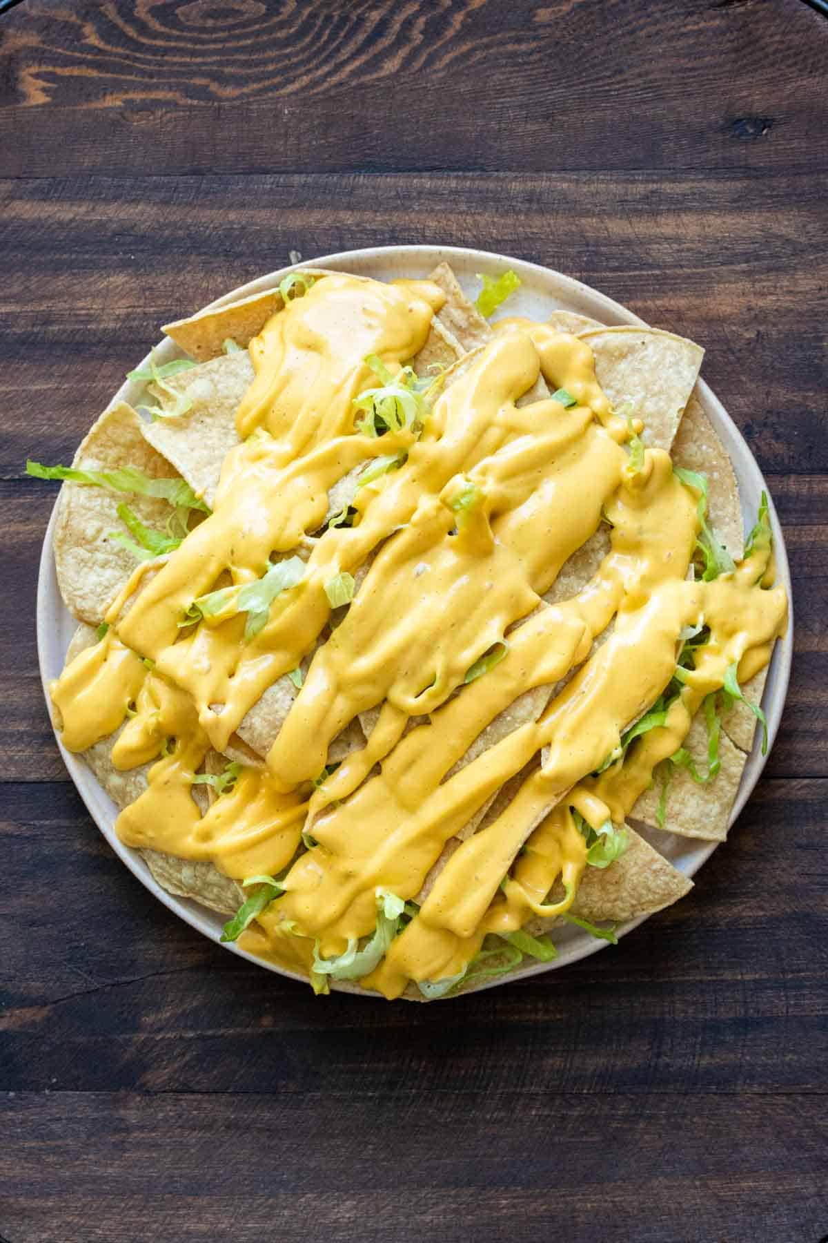 A plate piled with tortilla chips, lettuce and cheese sauce