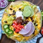 A plate of nachos with all the fixings on a striped towel with bowls of ingredients around it.