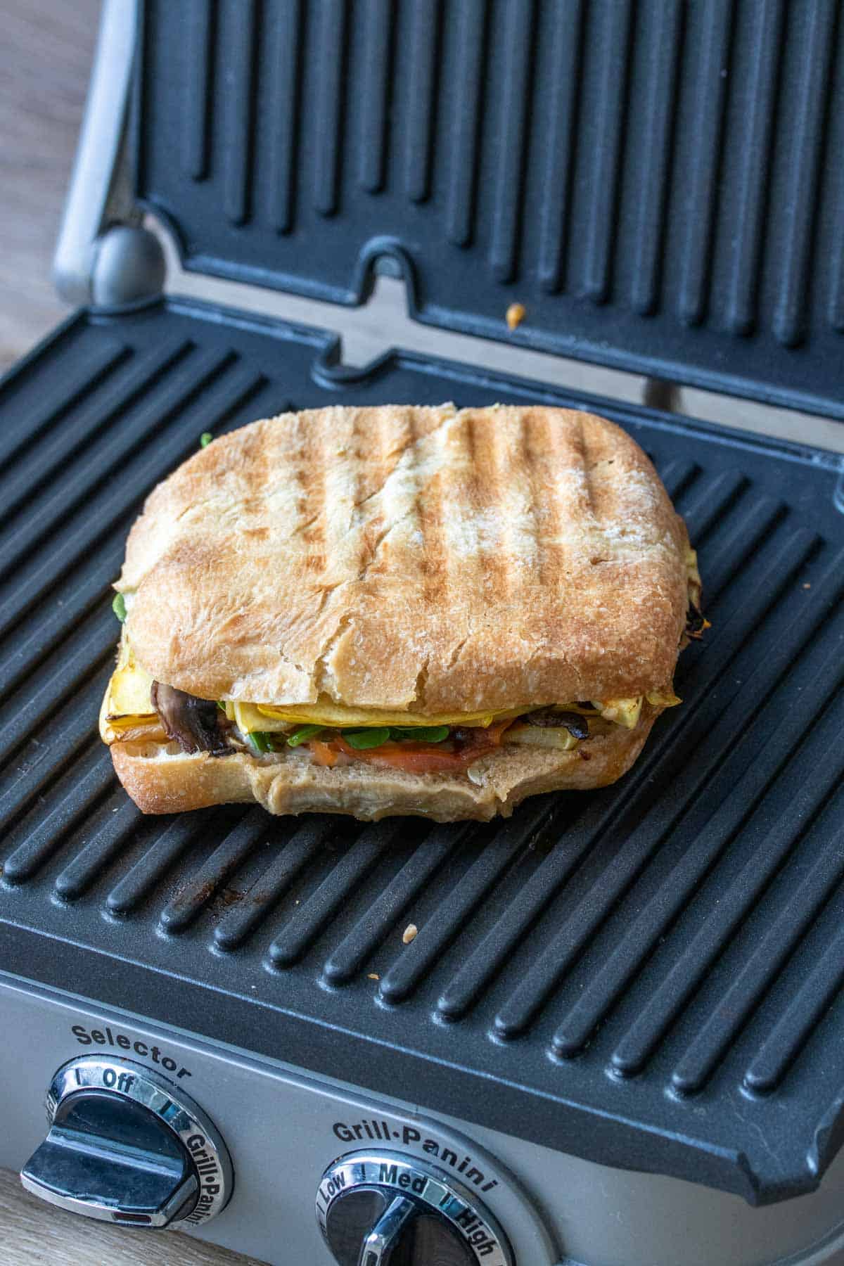 Front view of a panini with veggies being grilled on a panini press