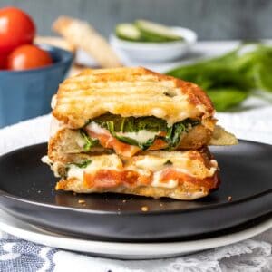 A black plate stacked with two halves of a veggie panini with spinach and tomatoes