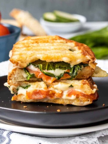 A black plate stacked with two halves of a veggie panini with spinach and tomatoes