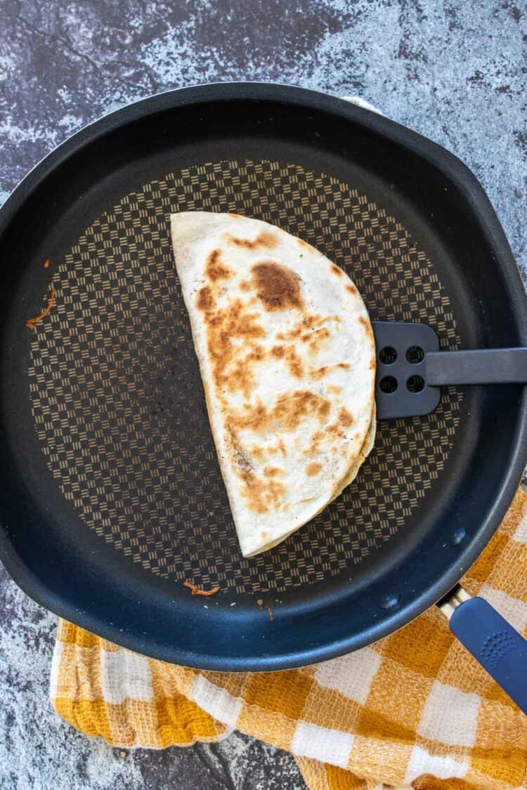 A spatula picking up a grilled quesadilla from a pan