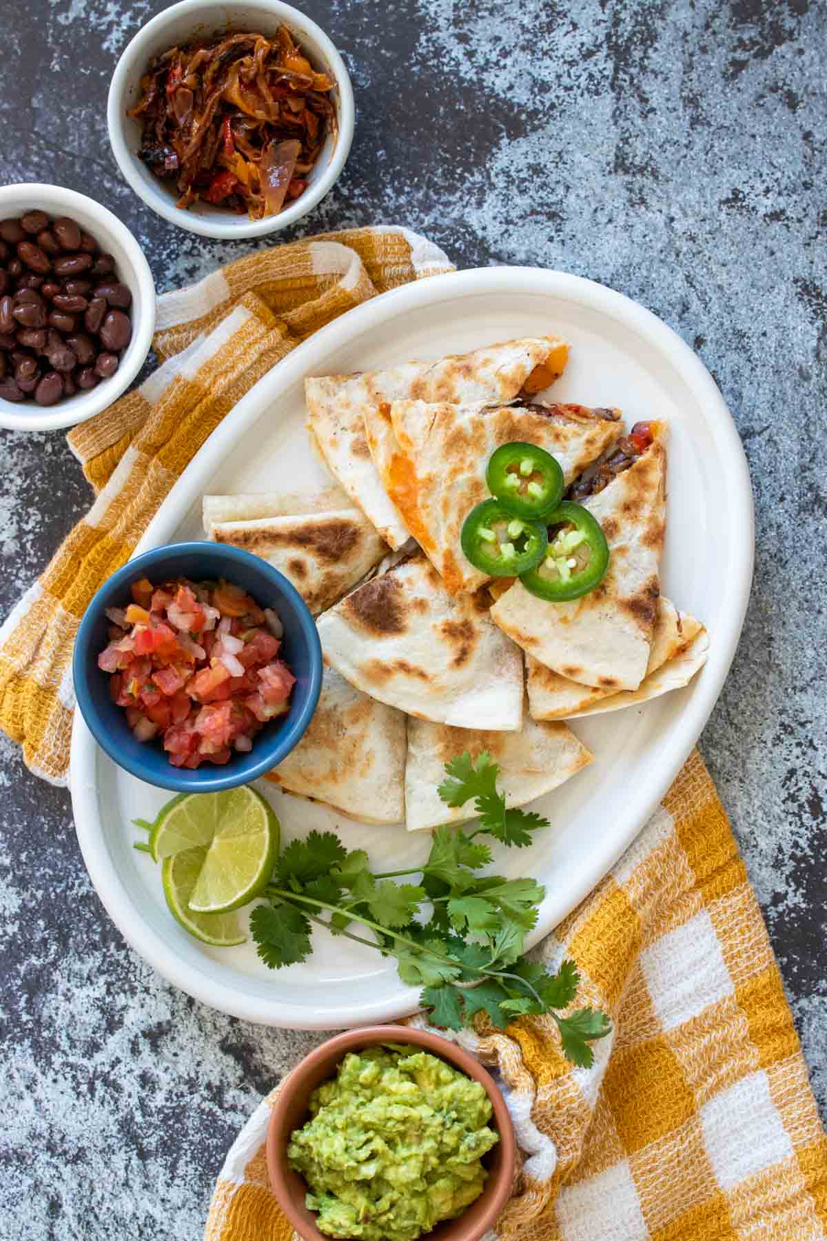 Top view of a white plate with quesadillas and a bowl of salsa on it on a grey stone background