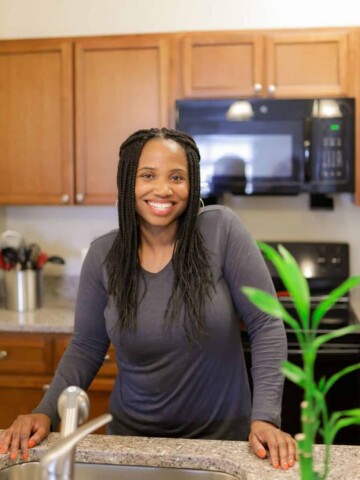 A black woman with long hair standing in her kitchen in front of the sink