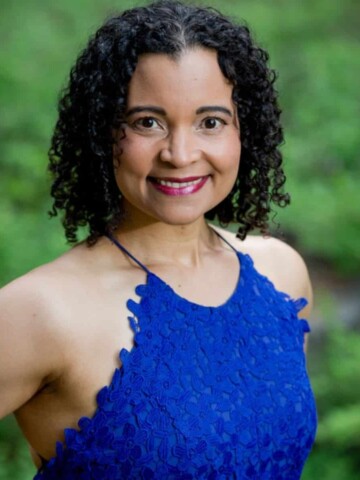 A black woman with shoulder length curly hair standing in a bright blue dress