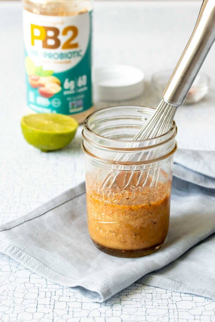 A glass jar with a brown sauce in it and a whisk