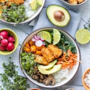 Top view of a bowl filled with rice, greens, veggies, tofu and surrounded by toppings