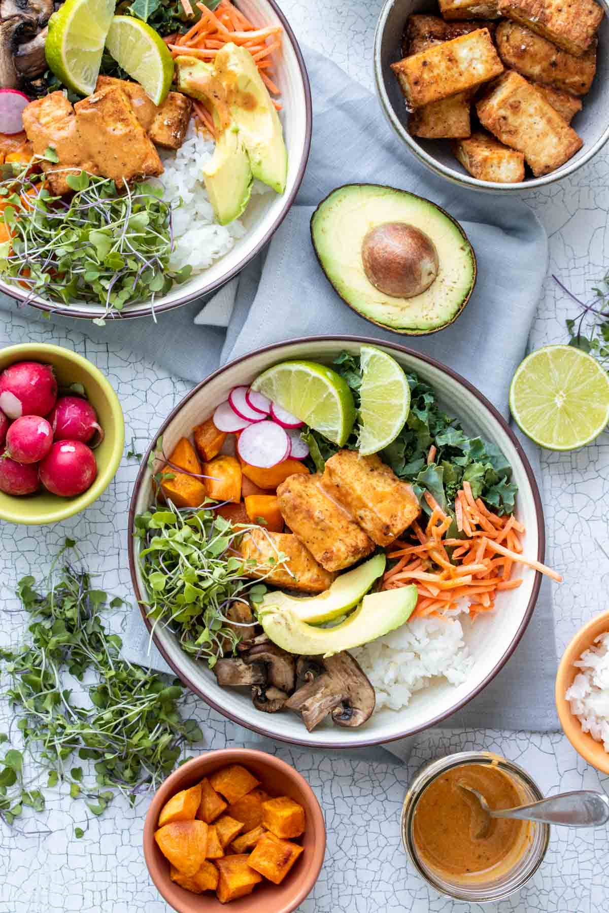 Top view of a bowl filled with rice, greens, veggies, tofu and surrounded by toppings