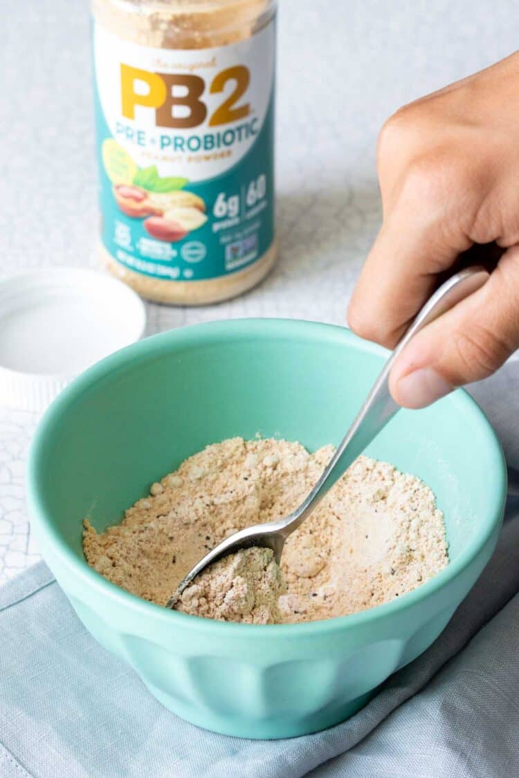 Hand mixing a powdered mixture in a turquoise bowl with a metal spoon