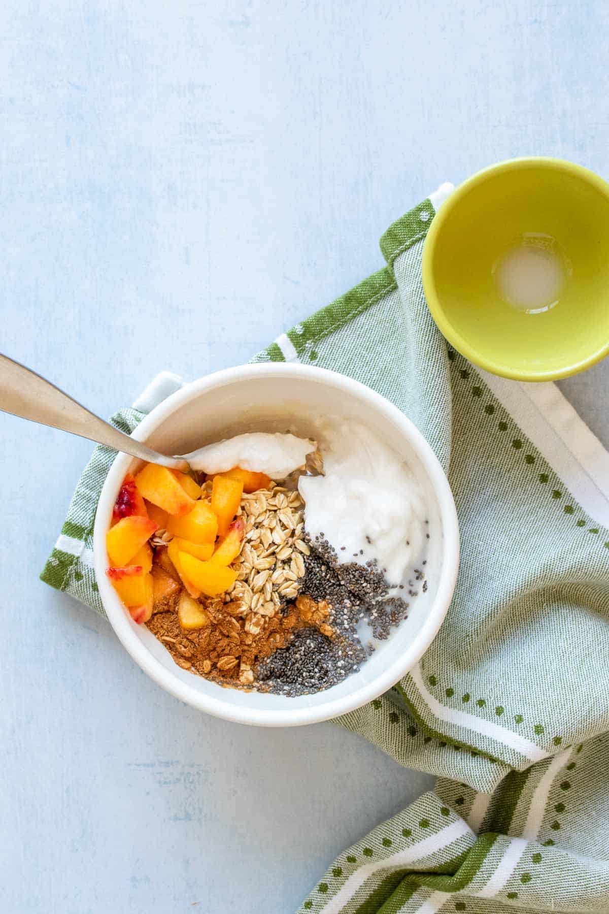 A spoon in a bowl with ingredients for peach overnight oats about to mix them