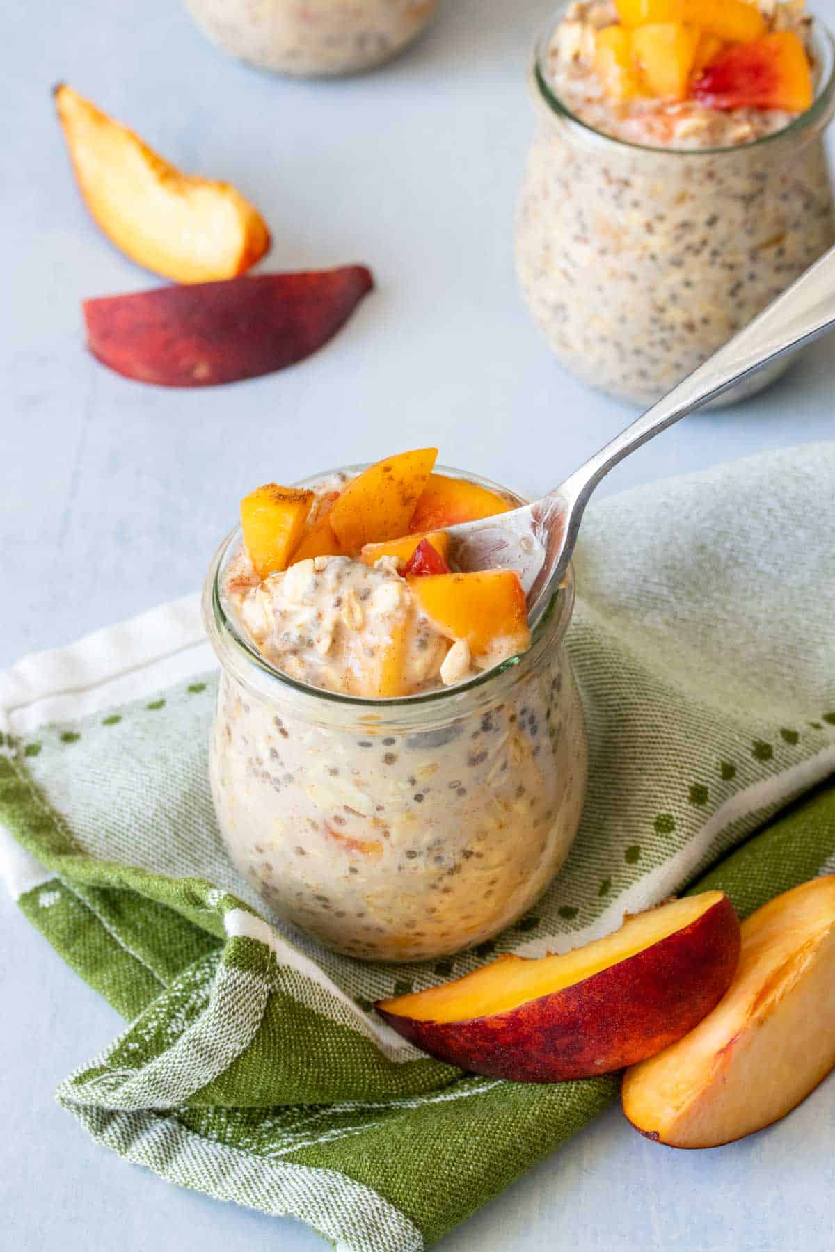 A spoon getting a scoop of peach oats out of a glass jar on a green towel