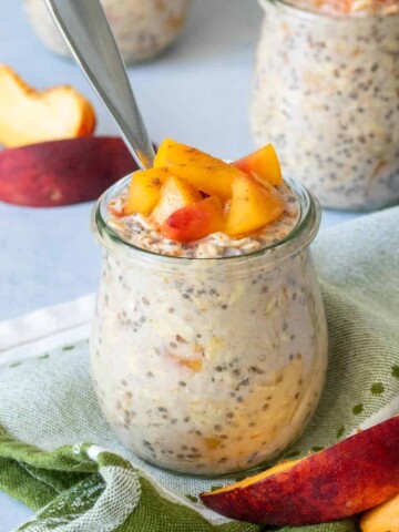 A glass jar with an oats and chia mixture topped with cut peaches sitting on a green towel