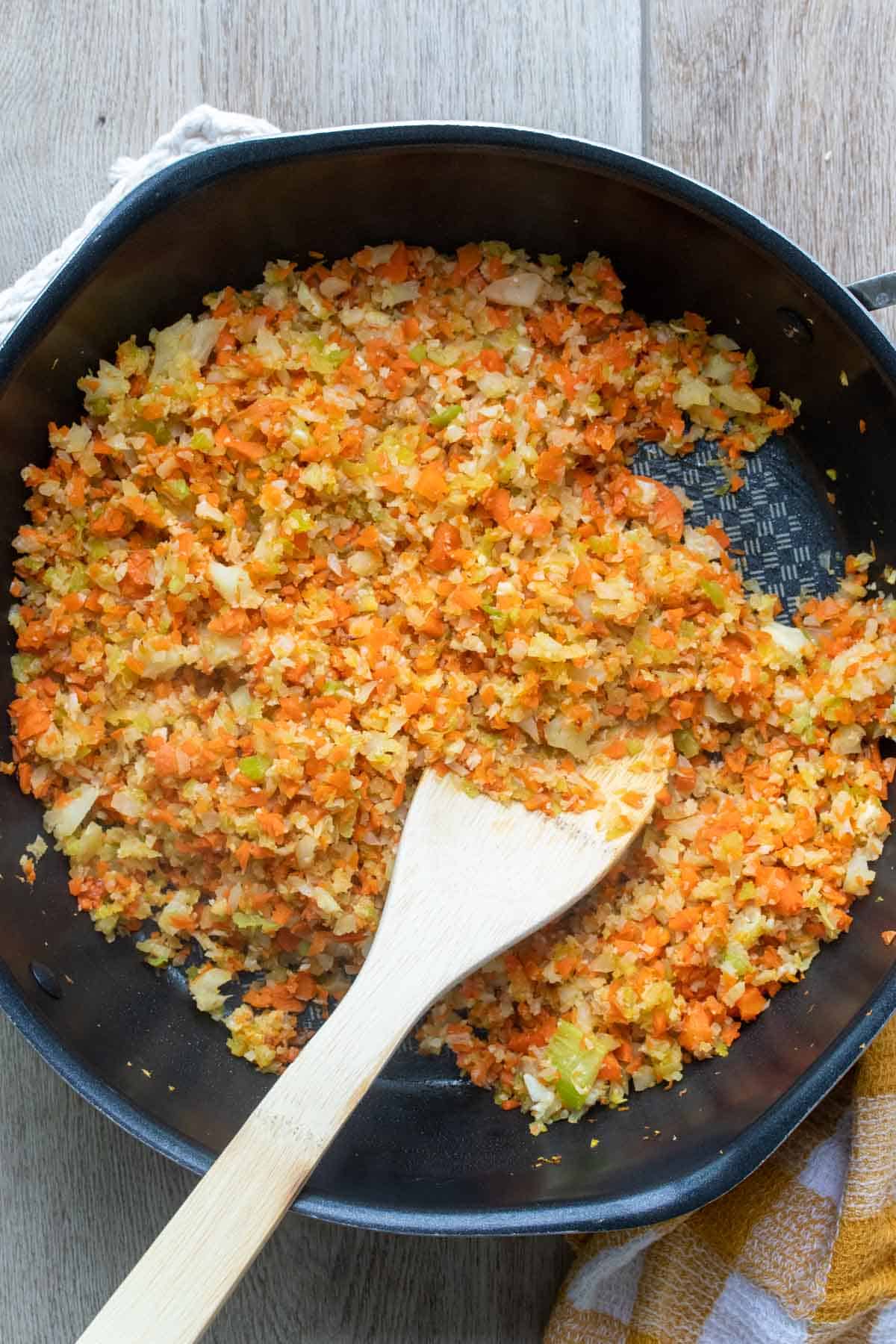 Wooden spoon mixing a mix of finely chopped veggies in a pan