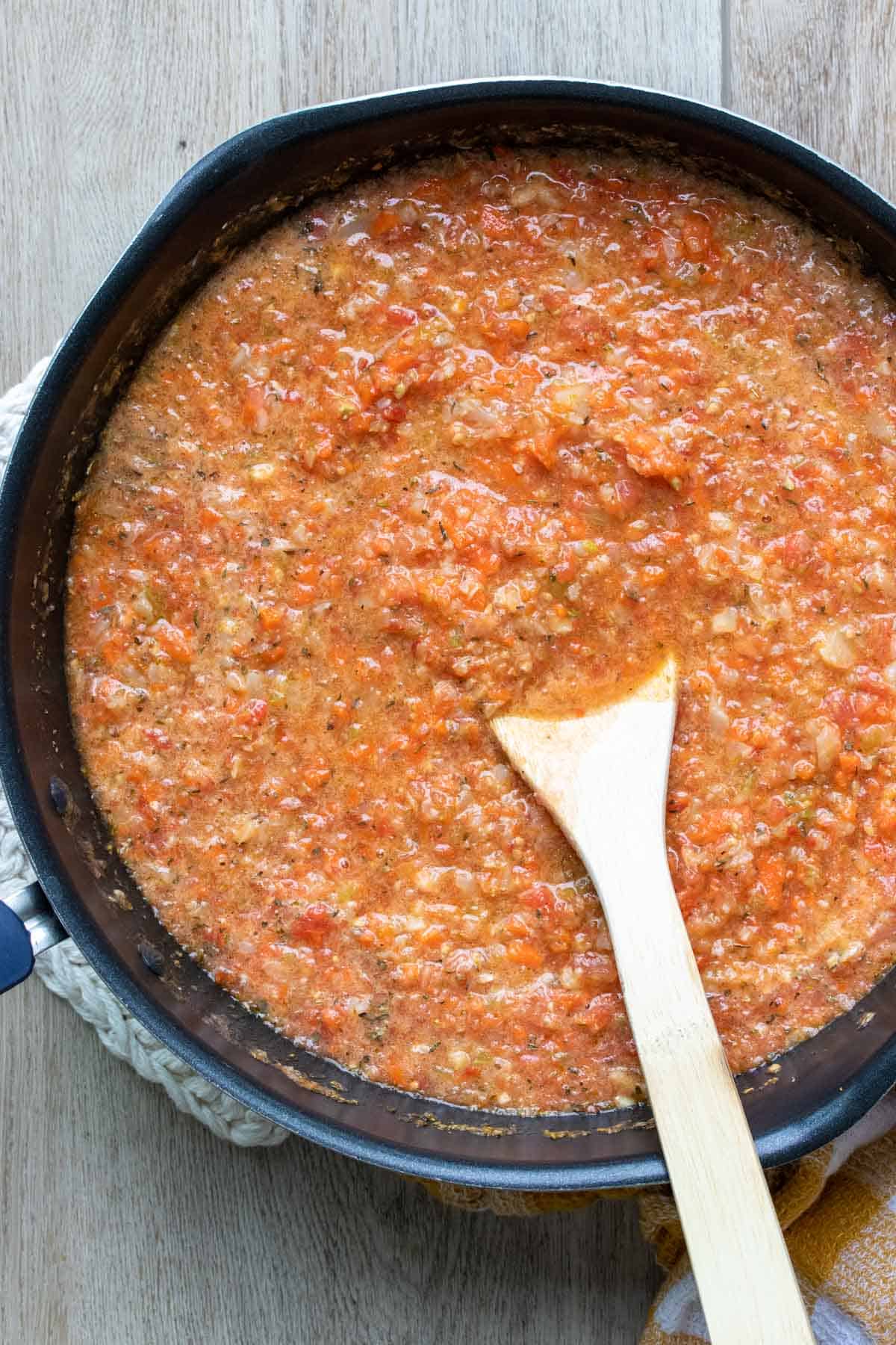 Wooden spoon mixing a veggie pasta sauce in a pan