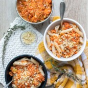 Three bowls on a wooden surface filled with penne pasta and veggie pasta sauce