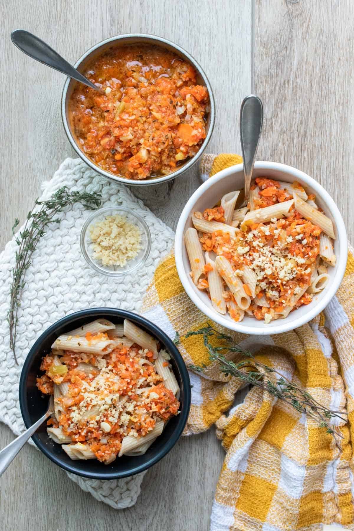 Three bowls on a wooden surface filled with penne pasta and veggie pasta sauce