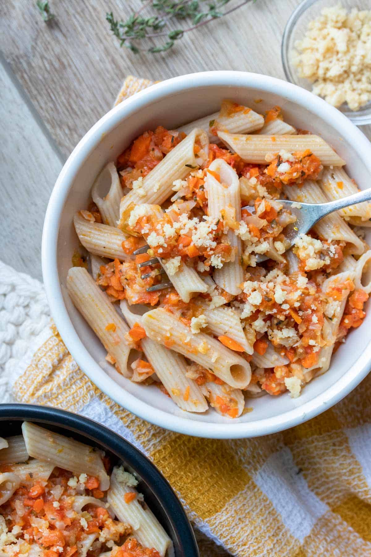 A fork getting a bite of penne pasta mixed with a veggie pasta sauce from a white bowl