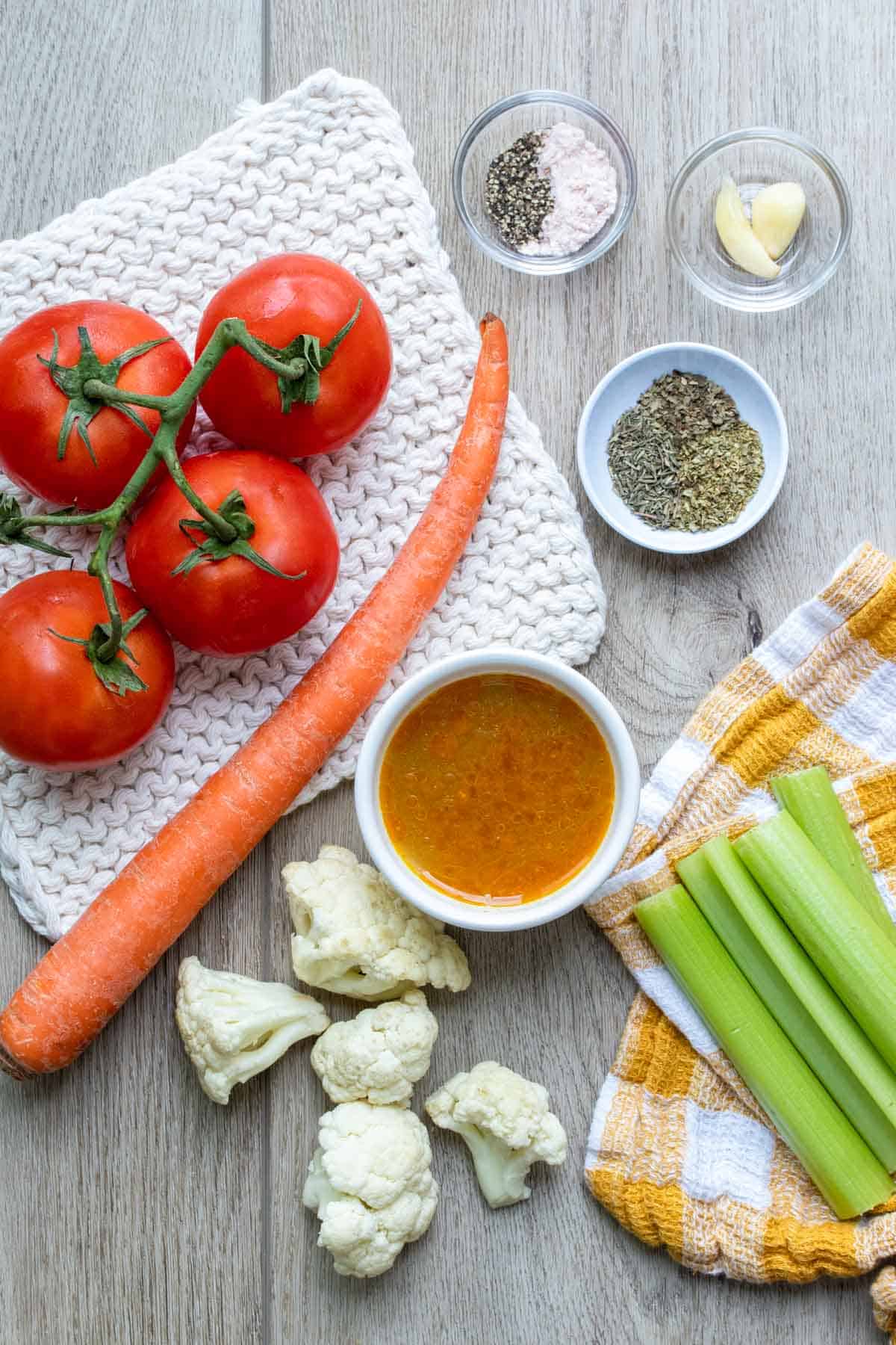 Tomatoes, carrot, cauliflower, celery, broth, garlic and spices on a wooden surface