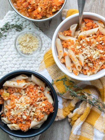 A black and white bowl of penne pasta and veggie pasta sauce on two towels