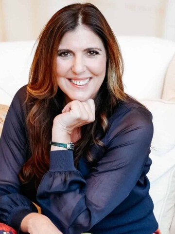 Woman with long brown hair and a blue long sleeve with hand under her chin