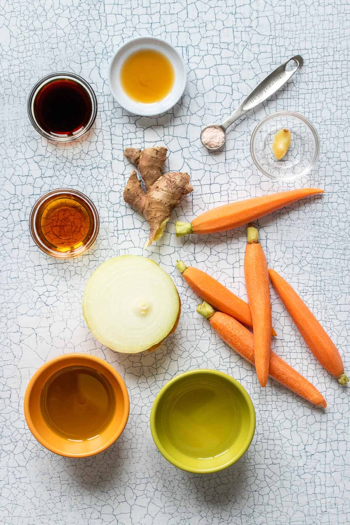 Top view of carrots, onion and ginger with bowls of different condiments to make a dressing