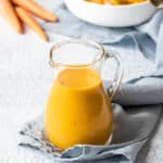 A small glass pitcher filled with an orange dressing on a folded up light blue towel