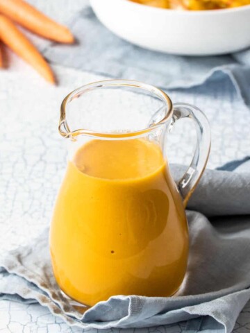 A small glass pitcher filled with an orange dressing on a folded up light blue towel