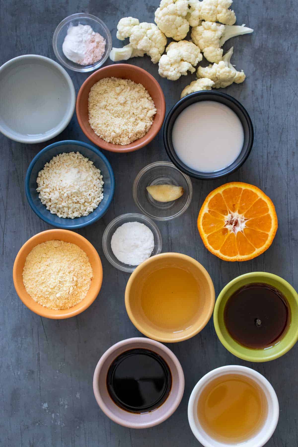 Top view of different colors bowls filled with liquids and flowers next to cauliflower, oranges and spices