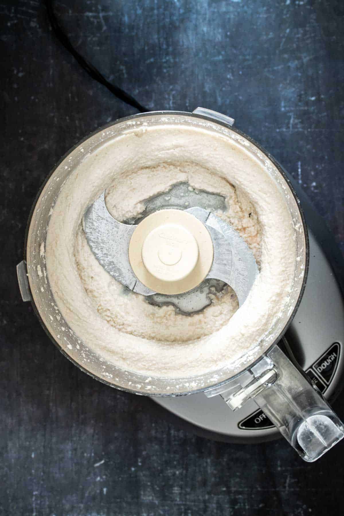 Top view of a food processor sitting on dark surface with a creamy mixture inside