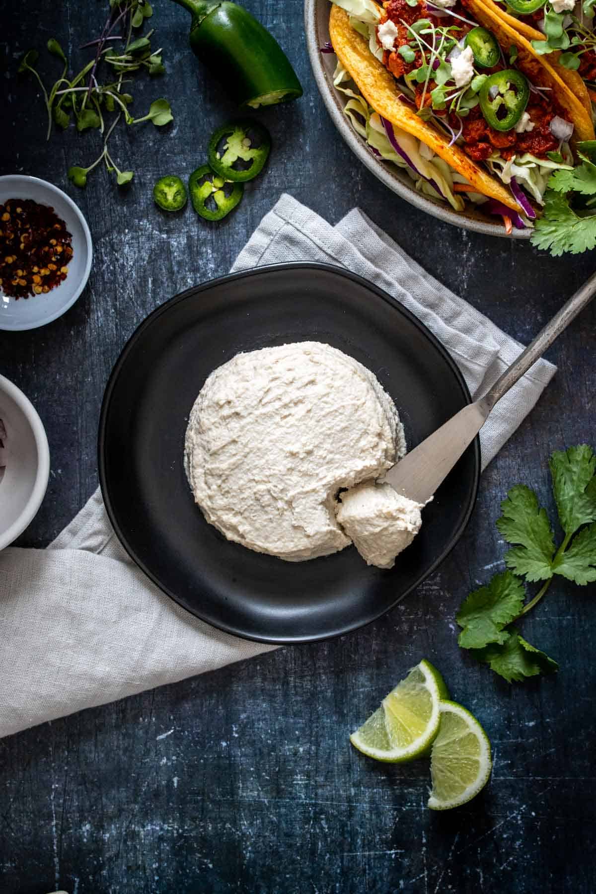 A silver knife taking a piece of cheese from a creamy cheese wheel sitting on a black plate