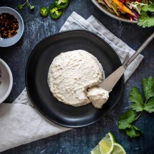 A round shape of thick creamy cheese with a knife taking some from it on a black plate.