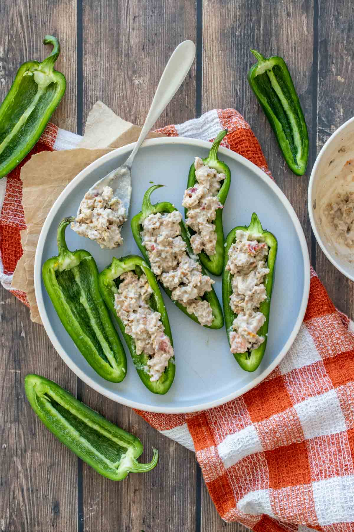 A grey plate with halved jalapenos stuffed with a sausage and cream mixture on a checkered towel