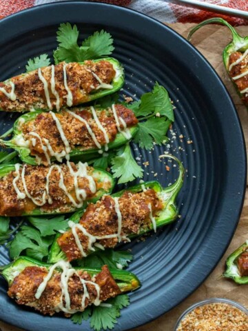 Five half pieces of jalapenos with a meaty filling and drizzled in a white cream on a black plate